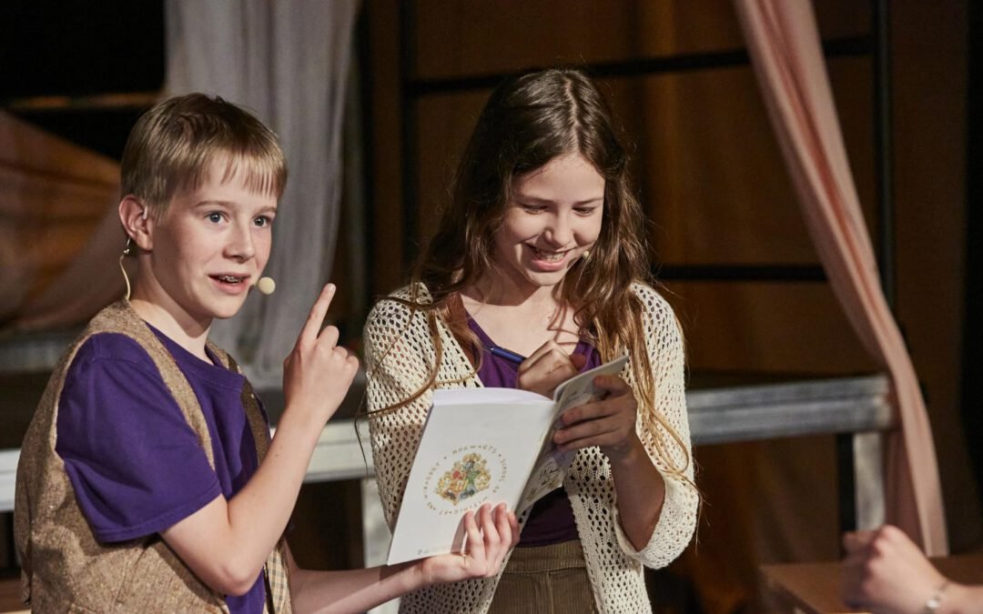 Lycantropia - Kein Weg zurück (2024) Zwei Kinder stehen nebeneinander, sie halten ein Buch, das eine zeigt mit dem Zeigefinger nach oben, das andere hält einen Stift und schreibt ins Buch