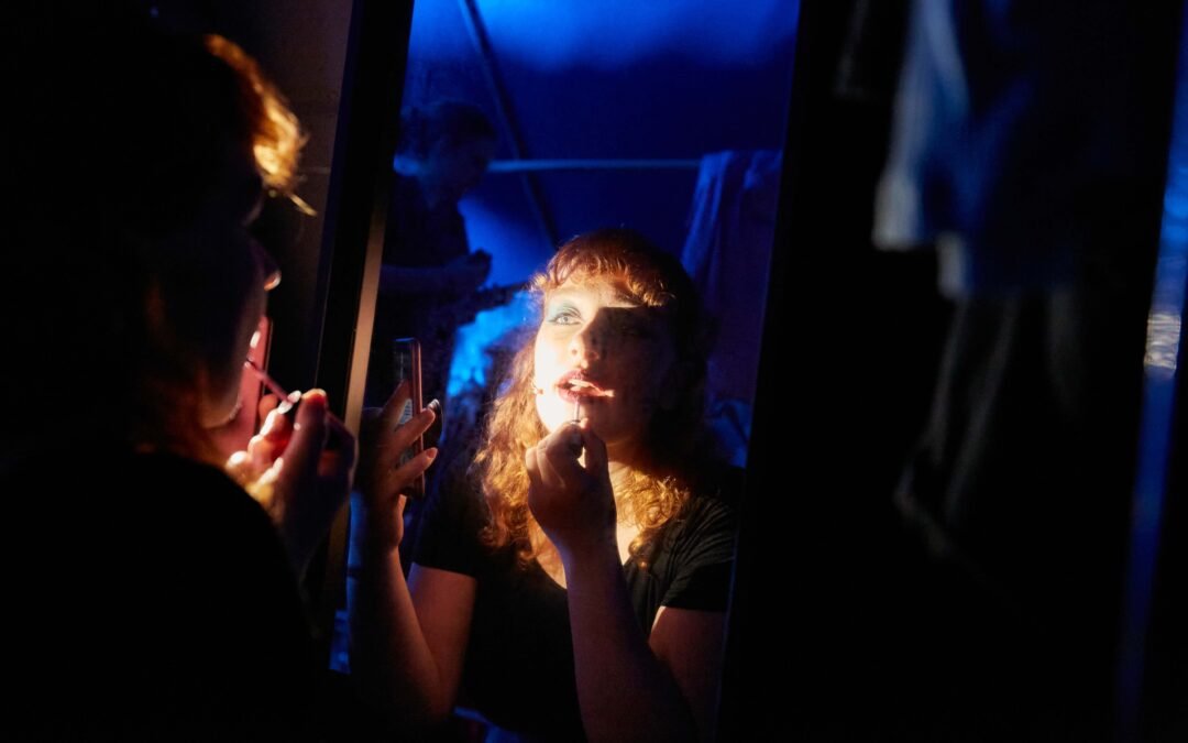 Backstage-10 Person mit lockigem Haar trägt vor einem Spiegel Lippenstift auf
