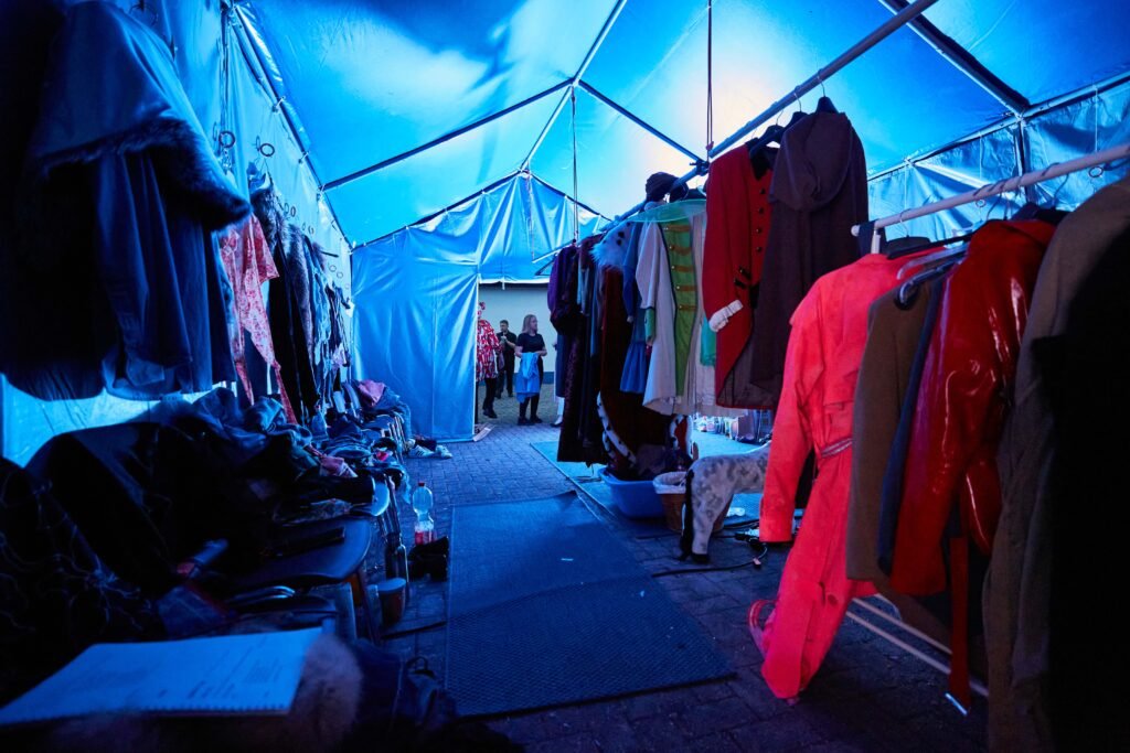Blick in einen Zeltgang mit an beiden Seiten hängenden Kostümen und zwei Personen im Hintergrund