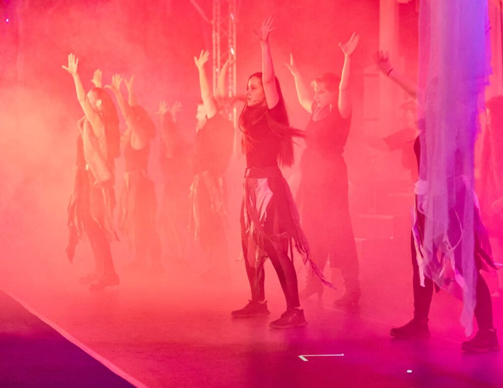 Lycantropia-07 Gruppe von Tänzern auf einer Bühne mit erhobenen Armen in rotem Bühnenlicht und Nebel